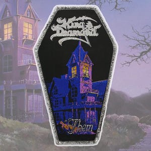 May include: A black coffin-shaped patch with a blue and purple haunted house illustration. The patch features the text "King Diamond" in silver and the word "Them" in gold. It has a silver border.