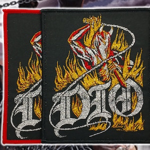 May include: Two black embroidered patches with a figure wielding a whip, set against flames, and the word "DIO" in a decorative font. One patch has a red border.