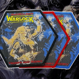 May include: Three hexagonal patches with the word "Warlock" in yellow. The patches have a blue background and a graphic of a woman and a figure. They have black, red, and blue borders, and the text "Triumph and Agony".