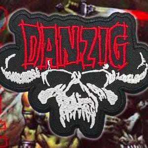 Könnte beinhalten: Gestickter schwarzer Aufnäher mit dem roten Wort "DANZIG" über einem weißen Totenkopf-Design. Der Aufnäher hat einen schwarzen Rand und ist wahrscheinlich für Kleidung oder Accessoires.