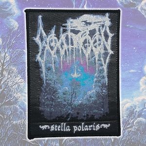 May include: A rectangular black fabric patch featuring a silver metallic embroidered band logo at the top. The center depicts a colorful forest scene with blue and purple hues, while the text "stella polaris" is embroidered in white at the bottom.