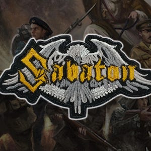 May include: Embroidered patch featuring the band name "Sabaton" in yellow gothic lettering, with a stylized eagle and wings design. The patch has a black border and is set against a blurred background of soldiers.