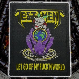 May include: A rectangular black embroidered patch featuring the yellow text TESTAMENT at the top and LET GO OF MY FUCK'N WORLD at the bottom. The center depicts a white skull with green wings above a blue and green globe held by purple hands.