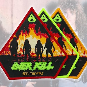Puede incluir: Tres parches bordados triangulares con fondo negro y un gráfico de fuego en amarillo y naranja. Cada parche muestra cuatro siluetas de músicos, el texto verde OVER KILL y el texto amarillo FEEL THE FIRE.