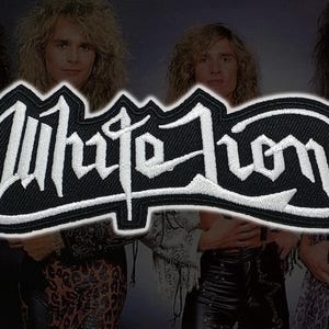 May include: A black and white embroidered patch featuring the band name White Lion in a stylized, gothic-inspired font. The design consists of white lettering with a thick white border against a solid black background, creating a high-contrast look.