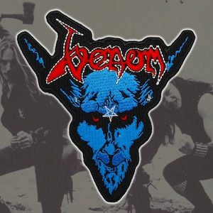 May include: Embroidered patch featuring the word "Venom" in red, stylized lettering above a blue demonic face with red eyes and a white star. The patch has a black border and is likely for a jacket or bag.