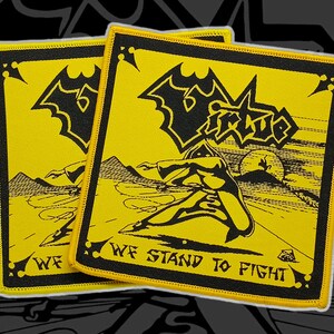 May include: Two yellow and black embroidered patches. Each patch features a black bat-like emblem and the word "Virtue" in a stylized font. The patches also display a figure in action and the text "WE STAND TO FIGHT".