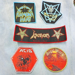 Könnte beinhalten: Fünf bestickte Stoffaufnäher mit Bandlogos und Grafiken. Oben links: Diamond Head. Oben rechts: Running Wild. Mitte: Venom mit zwei Ziegenköpfen. Unten links: Acid mit einer Kreaturengrafik. Unten rechts: Runder Angel Witch Aufnäher.
