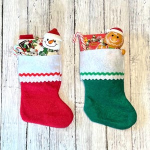 May include: Two Christmas stockings filled with gifts. The stocking on the left is red with white trim and contains a snowman, candy canes, and other small gifts. The stocking on the right is green with white and green trim and contains a gingerbread man, candy canes, and other small gifts.