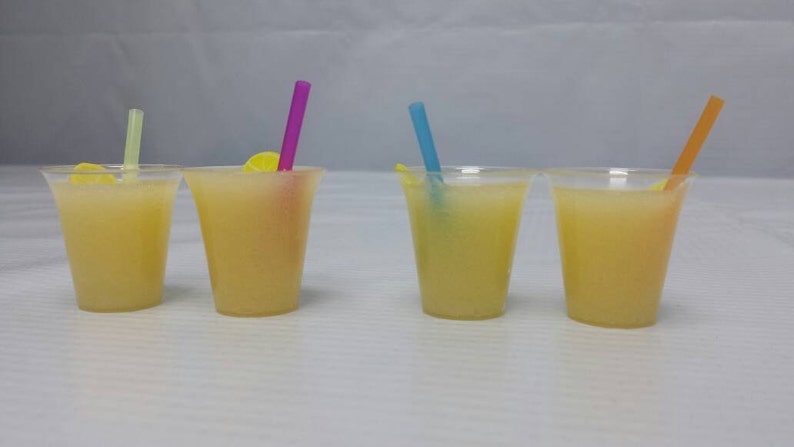 May include: Four clear plastic cups filled with a yellow liquid, each with a different colored straw. The straws are pink, blue, green, and orange.