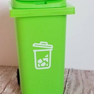 May include: A bright green plastic trash can with a white recycling symbol on the front. The can has a lid and a small wheel on the bottom.