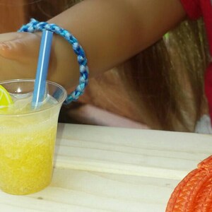 May include: A clear plastic cup with a yellow lemon slice and a blue straw filled with a yellow, bubbly drink. The cup is sitting on a wooden table.