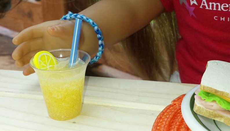 May include: A clear plastic cup with a yellow lemon slice and a blue straw filled with a yellow, bubbly drink. The cup is sitting on a wooden table.