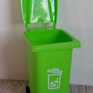May include: A bright green plastic trash can with a white recycling symbol and a black wheel. The lid is open.