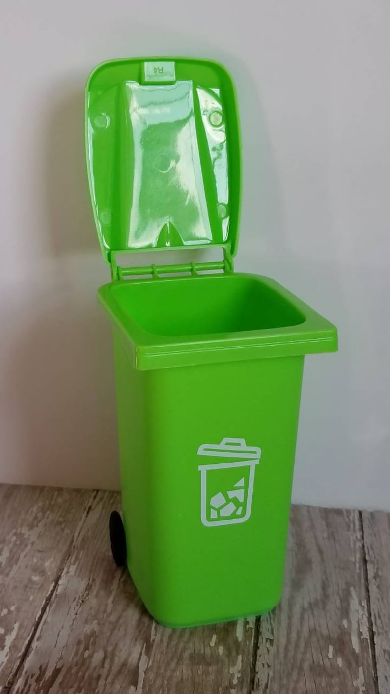 May include: A bright green plastic trash can with a white recycling symbol and a black wheel. The lid is open.