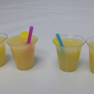 May include: Four clear plastic cups filled with a light yellow liquid, each with a straw and a lemon slice. The straws are different colors: green, purple, blue, and orange.
