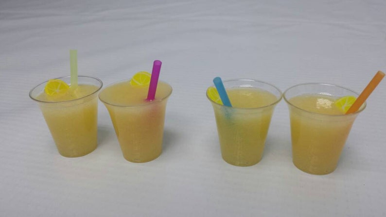 May include: Four clear plastic cups filled with a light yellow liquid, each with a straw and a lemon slice. The straws are different colors: green, purple, blue, and orange.
