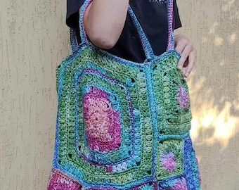 May include: A large, colorful crocheted tote bag with a geometric pattern in shades of green, blue, pink, and white. The bag has two long straps and is made with a variety of stitches.