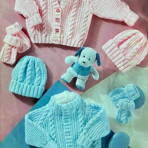 May include: A collection of knitted baby clothing in soft pastel colors. The image features a pink cardigan, a blue sweater, matching hats, mittens, and a scarf. A plush puppy toy is also included. The text "Wondersoft" and "Stylecraft" are visible.