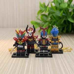 May include: Four colorful action figure keychains. The figures are in various colors, including red, gold, blue, and black. Each figure is attached to a small black base and has a gold-colored keychain ring.