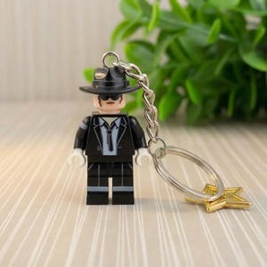 May include: A white ceramic mug with a black handle and the text "But First, Coffee" in a black, handwritten-style font. The mug is on a white surface.