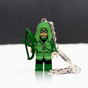 May include: A Green Arrow Lego keychain. The figure is wearing a green hood, mask, and costume, and holds a green bow and arrow. The keychain has a silver chain and clasp.