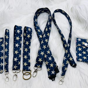 May include: A collection of navy blue accessories with a gold star pattern. The set includes a phone case, wristlets, lanyards, and a small pouch. Each item has a silver or gold-tone clasp or ring.