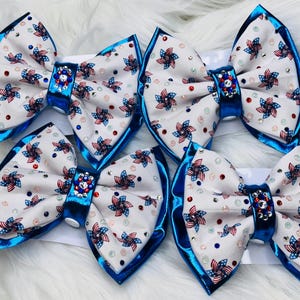 May include: Six patriotic hair bows. Each bow features a white fabric with red, white, and blue pinwheel and star patterns. The bows have a blue velvet trim and a jeweled center. Perfect for Independence Day.