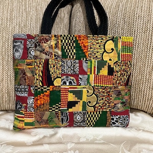May include: A patchwork tote bag with a variety of colorful African fabric patterns. The bag features a mix of red, green, yellow, and black geometric designs. It has black rope handles and a rectangular shape.