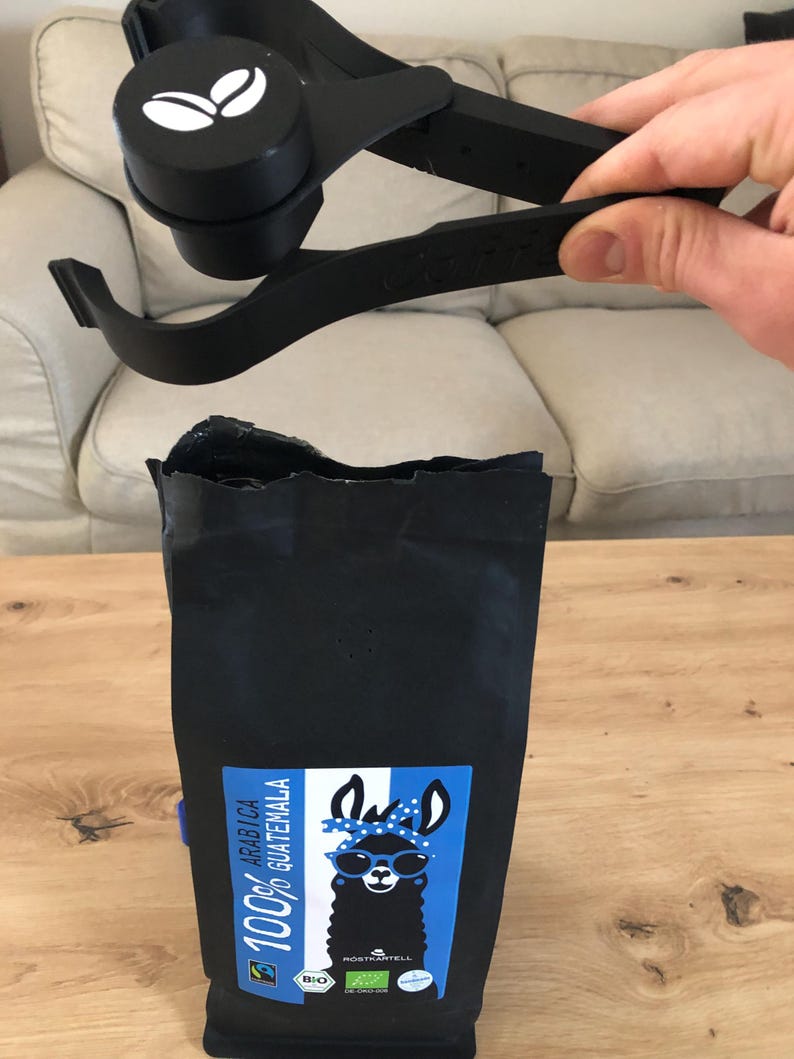 Puede incluir: Una bolsa de caf&eacute; negra con una llama con gafas de sol en la parte delantera. La bolsa est&aacute; etiquetada "100% Arabica Guatemala".