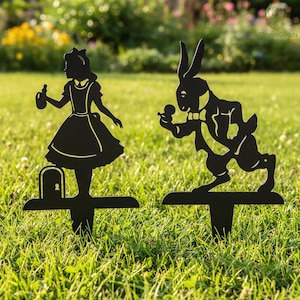 Peut inclure: Deux piquets de jardin en métal noir représentant les silhouettes d'Alice et du Lapin Blanc d'Alice au pays des merveilles. Alice tient une bouteille et le lapin un gousset. Conçus pour être plantés dans un jardin ou une pelouse.