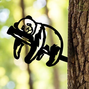 Może przedstawiać: Czarna metalowa sylwetka pandy odpoczywającej na gałęzi, przymocowana do pnia drzewa. Panda jest w zrelaksowanej pozie, z głową opartą na gałęzi. Tło jest rozmyte, zielone i brązowe.