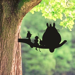 May include: Black silhouette of characters from a popular animated film, perched on a tree branch. The figures include a large, round creature with pointed ears, a smaller figure, and a rabbit-like character. The background is a blurred green.