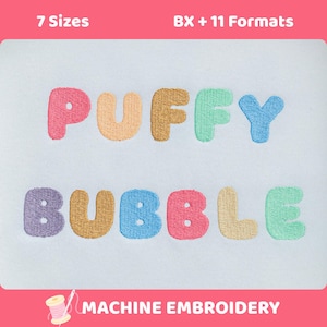 Op de afbeelding: Een borduurontwerp met de woorden PUFFY BUBBLE gestikt in kleurrijke, afgeronde letters op een lichtblauwe stoffen achtergrond. De tekst bevat roze, beige, bruine, groene, blauwe, paarse en gele garenkleuren in een speels lettertype.