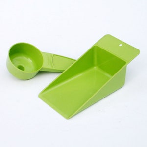 May include: Two green plastic kitchen scoops. One is a measuring cup shape, and the other is a rectangular scoop with a handle. Both are made of a solid, bright green plastic.