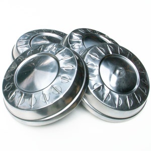 May include: Four silver hubcaps with a raised design and a central dome. The hubcaps have a shiny, reflective finish.