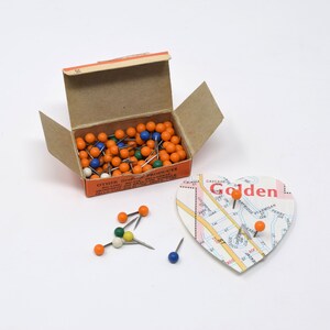 May include: A box of orange and white push pins with a map of Golden, Colorado, with red text that says "Golden" and a few push pins stuck in the map.