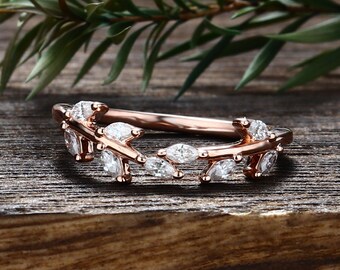 Puede incluir: Un anillo de oro rosa con una banda en forma de enredadera, adornado con piedras claras de talla marquesa dispuestas como hojas en la parte superior. El metal tiene un acabado pulido y las piedras siguen un patrón repetitivo a lo largo del aro.