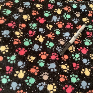 May include: Black fabric with a colorful paw print pattern. The paw prints are in shades of red, orange, yellow, green, and blue. A black and silver Sharpie marker rests on the fabric.