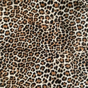 May include: A close-up view of a leopard print fabric. The pattern consists of black, brown, and tan spots on a cream background. The spots are of varying sizes and shapes, giving a textured look. The fabric is suitable for clothing or home furnishings.