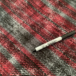 May include: Close-up of a fabric with a diagonal plaid pattern in red, black, gray, and white. A black Sharpie marker is in the lower right corner. The fabric has a textured appearance.