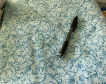 May include: Close-up of a fabric with a light blue and white floral pattern. A black pen with a rubber grip rests on the fabric, which is folded. The fabric has a soft, textured appearance, with a repeating design of swirling vines and flowers.