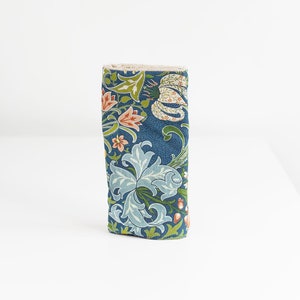 May include: A blue fabric eyeglass case with a floral pattern featuring green leaves, pink and orange flowers, and white lilies.