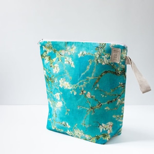May include: A turquoise zippered pouch with a floral print featuring white blossoms and green branches. The pouch has a beige fabric handle.
