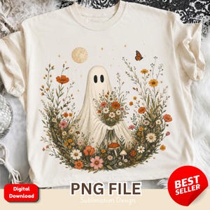 Könnte beinhalten: Ein cremefarbenes T-Shirt mit einer Grafik eines weißen Geistes, der einen großen Strauß bunter Wildblumen hält. Das Design zeigt einen goldenen Mond, einen kleinen Schmetterling sowie verschiedene orange, rosa und weiße Blumen.