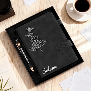 May include: A black journal and pen set in a gift box. The journal features a floral design and the name "Selena" in white. The pen has gold-colored accents and the text "YOUR TEXT LOGO HERE". A cup of coffee is in the background.