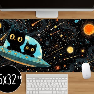 Op de afbeelding: Zwarte bureaumat met een ruimtethema. Twee zwarte katten zitten in een blauw ruimteschip, omringd door sterren, planeten en vallende sterren. De mat is 40,6 x 81,3 cm en bevat een toetsenbord en muis.