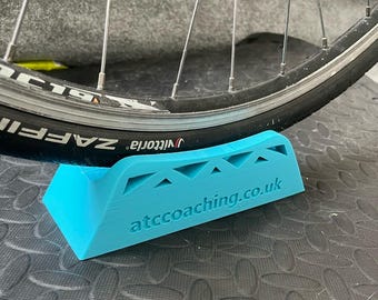 May include: A light blue plastic bike wheel stand with the text "attcoaching.co.uk" printed on it.