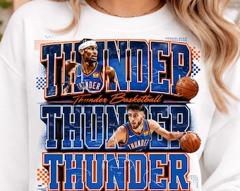 May include: White sweatshirt featuring the word "THUNDER" in blue and orange block letters. The design includes images of basketball players and basketballs. The words "Thunder Basketball" are also present.