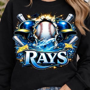 Può includere: Felpa nera con un design a tema baseball. La grafica include una palla da baseball, caschi, mazze e onde d'acqua, con la scritta "RAYS" in blu e bianco. Il design ha un tema sportivo.